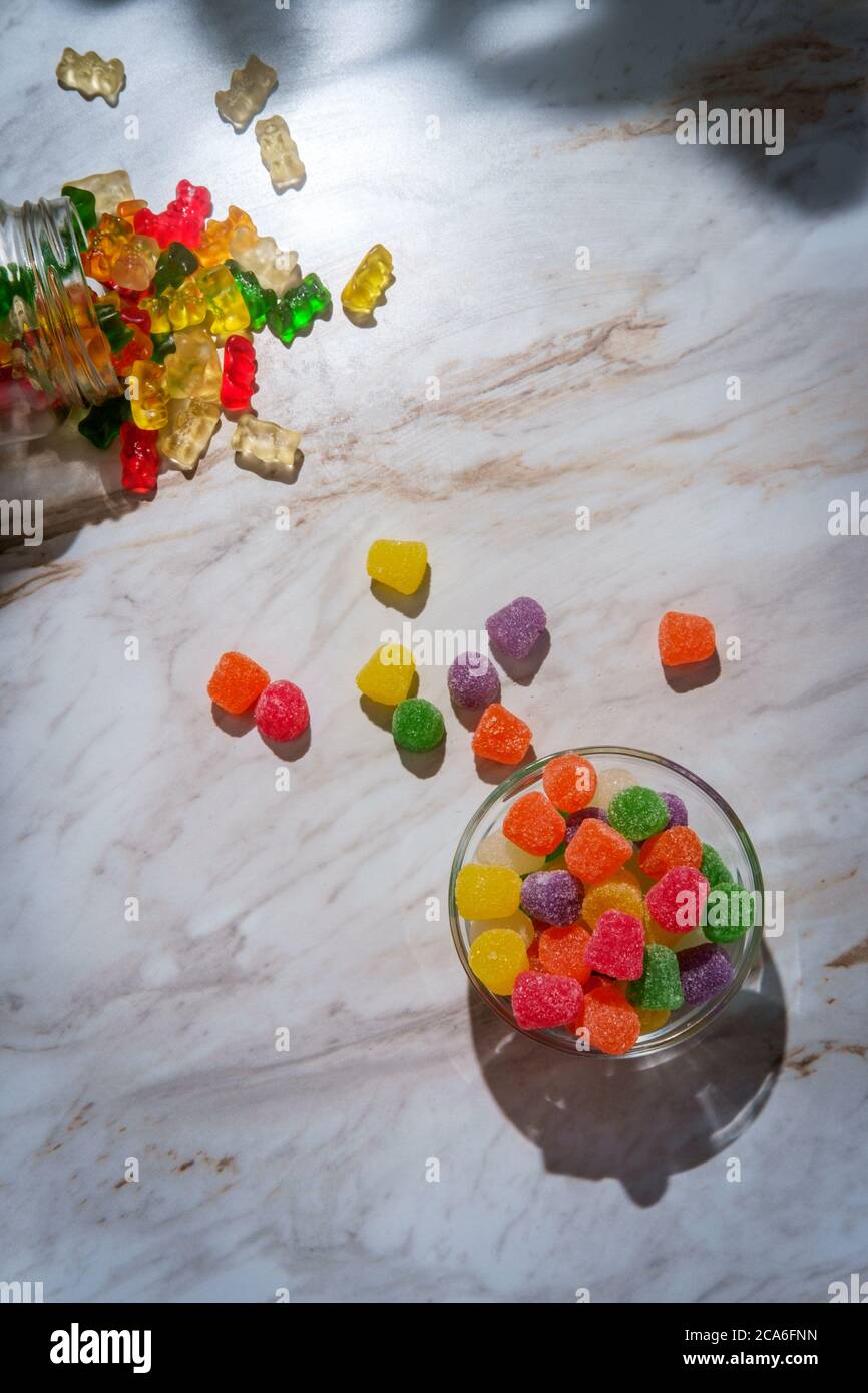 Mit granuliertem Zucker beschichtete Bonbons mit verschütteten Gläschen Gummibärchen im Hintergrund Stockfoto