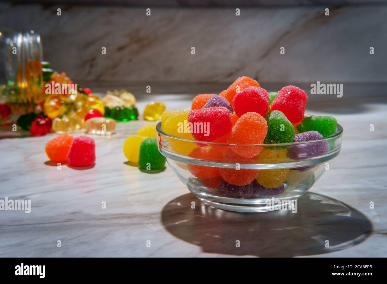 Mit granuliertem Zucker beschichtete Bonbons mit verschütteten Gläschen Gummibärchen im Hintergrund Stockfoto
