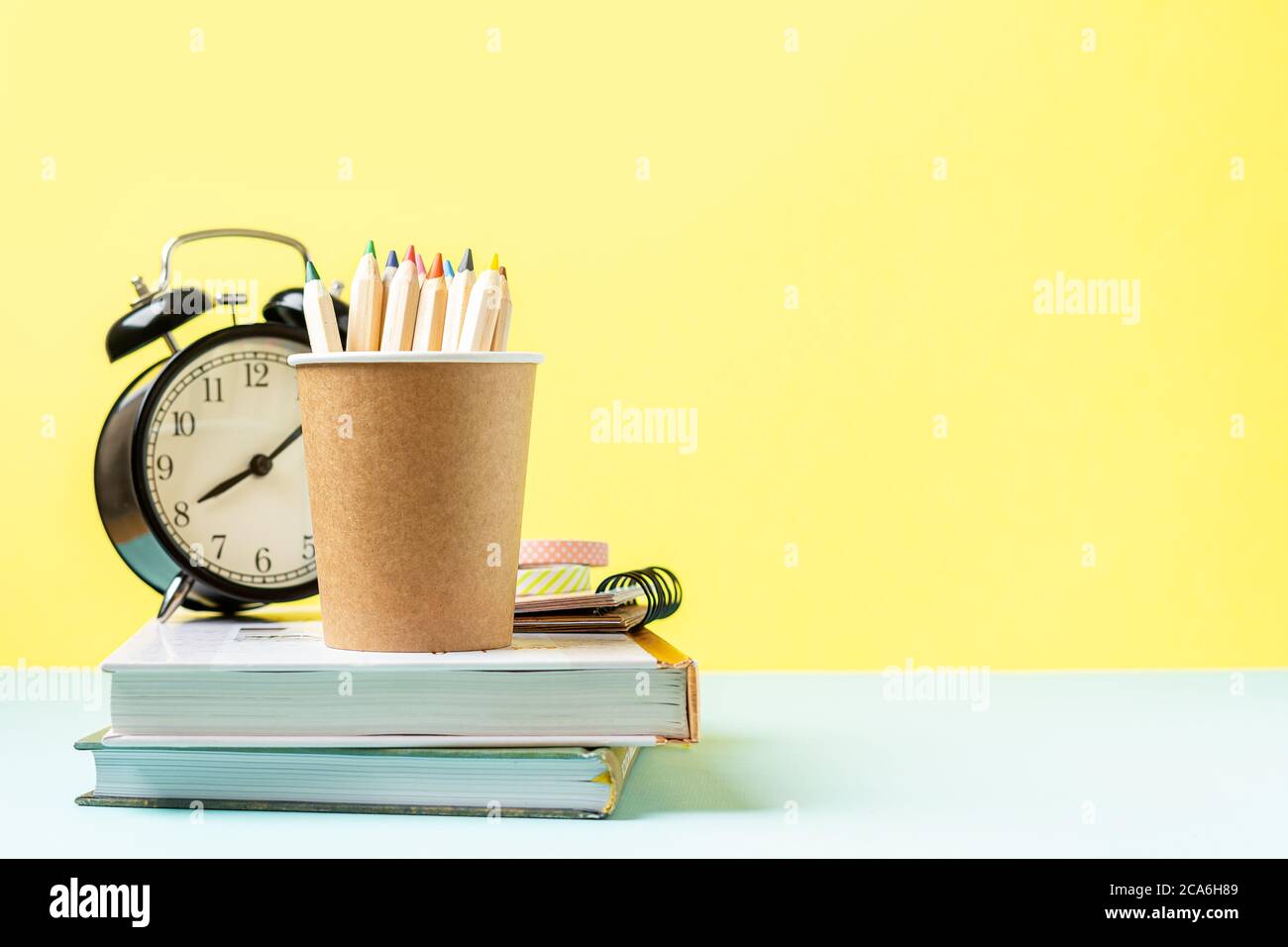 Back to School Banner mit schwarzem Wecker, Büchern und Bleistift. Schulbedarf, andere Elemente in gelber Minze leerer Hintergrund mit Kopierraum Stockfoto