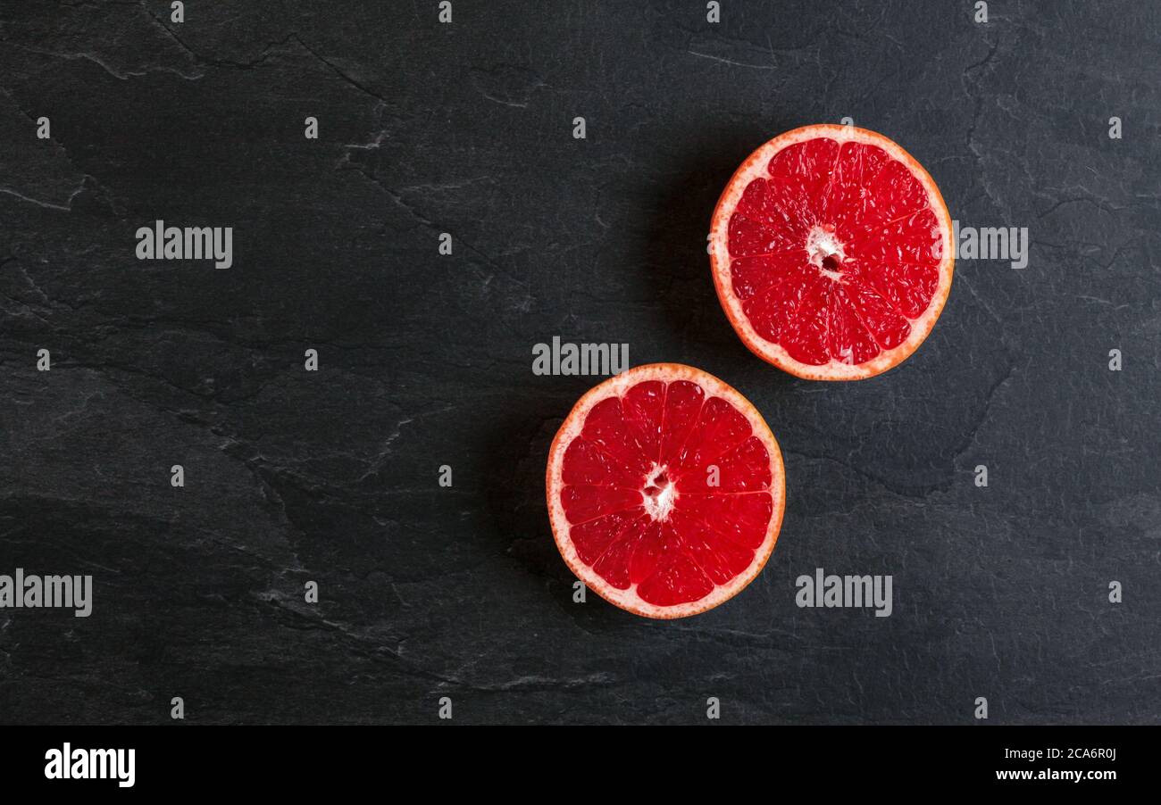 Flach legen Foto - rosa Grapefruit in zwei Hälften geschnitten, auf schwarzem Schiefertafel Stockfoto