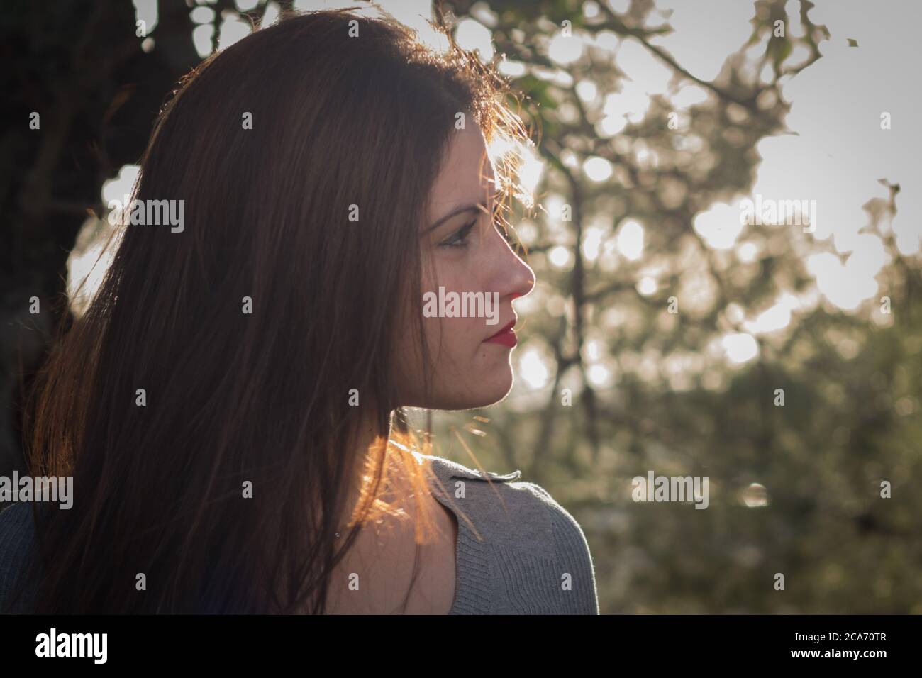 Hintergrundbeleuchtetes Profil eines hübschen jungen spanischen Mädchen posiert in Ein Wald Stockfoto