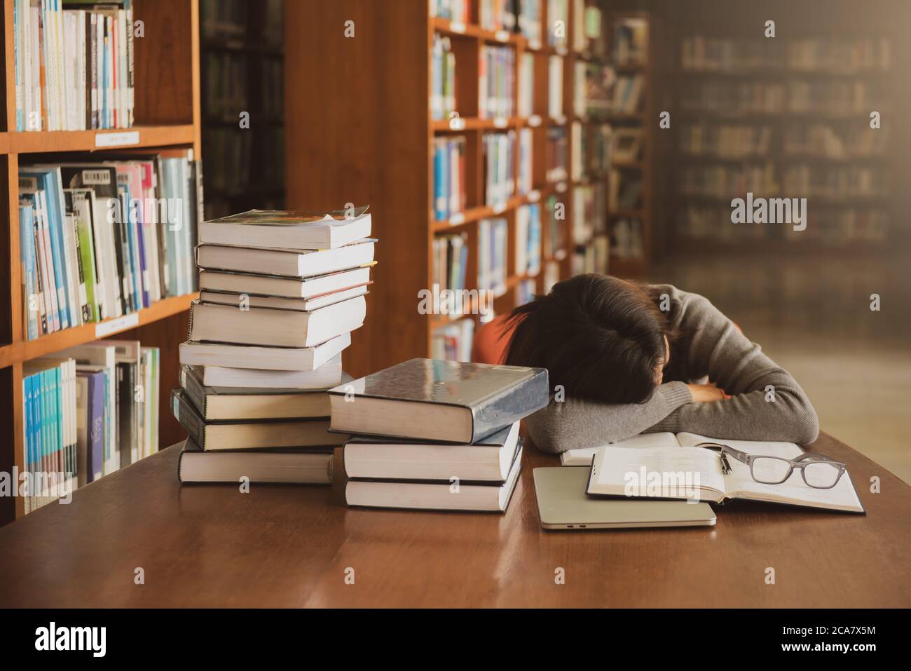 Müde erschöpfte junge Student schlafen auf dem Tisch mit Buch geöffnet in der Bibliothek. Stockfoto