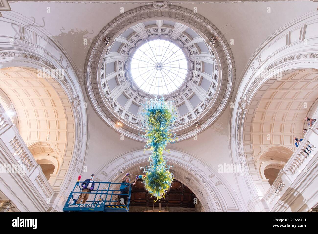 Museumstechniker Andy Monk reinigt den 27 Meter langen Rotunda-Kronleuchter von Dale Chihuly, der aus 1,300 blauen und grünen Glaselementen besteht, im Victoria and Albert Museum in London, während er sich auf die Wiedereröffnung am 6. August vorbereitet. Stockfoto