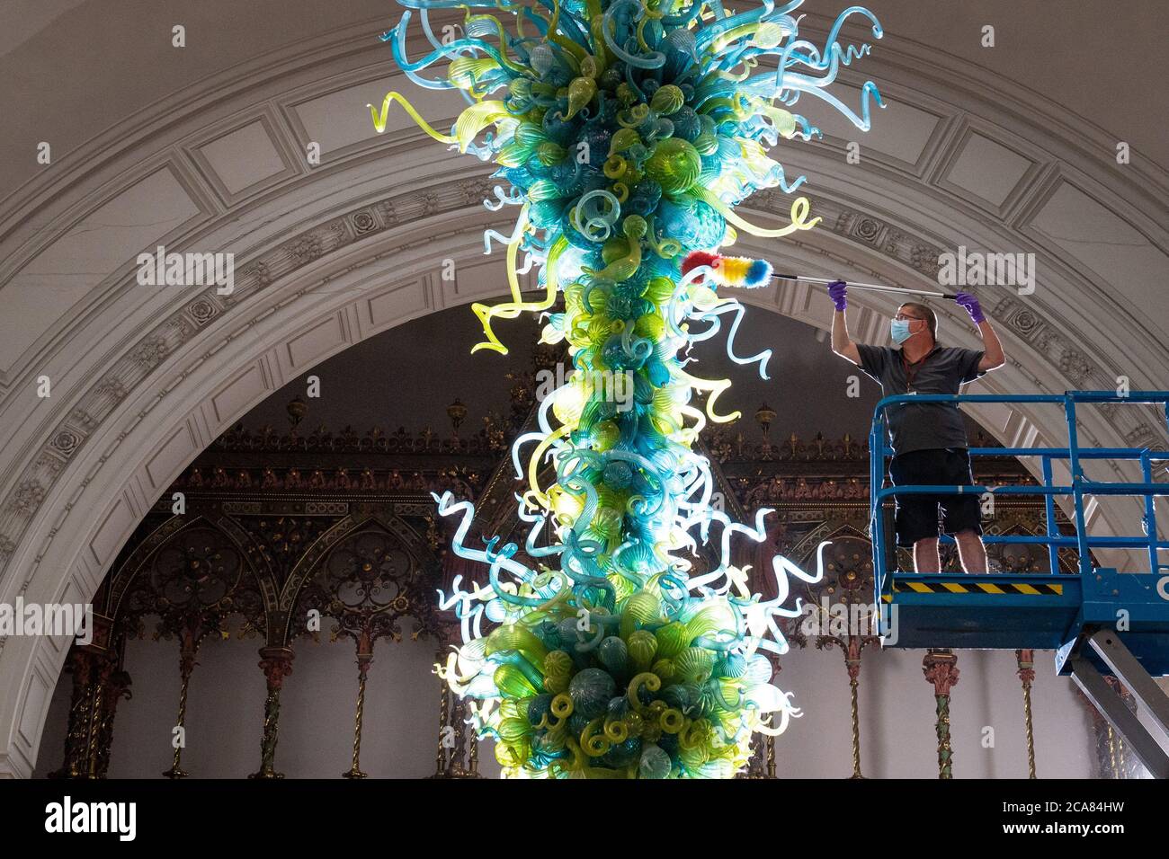 Museumstechniker Andy Monk reinigt den 27 Meter langen Rotunda-Kronleuchter von Dale Chihuly, der aus 1,300 blauen und grünen Glaselementen besteht, im Victoria and Albert Museum in London, während er sich auf die Wiedereröffnung am 6. August vorbereitet. Stockfoto