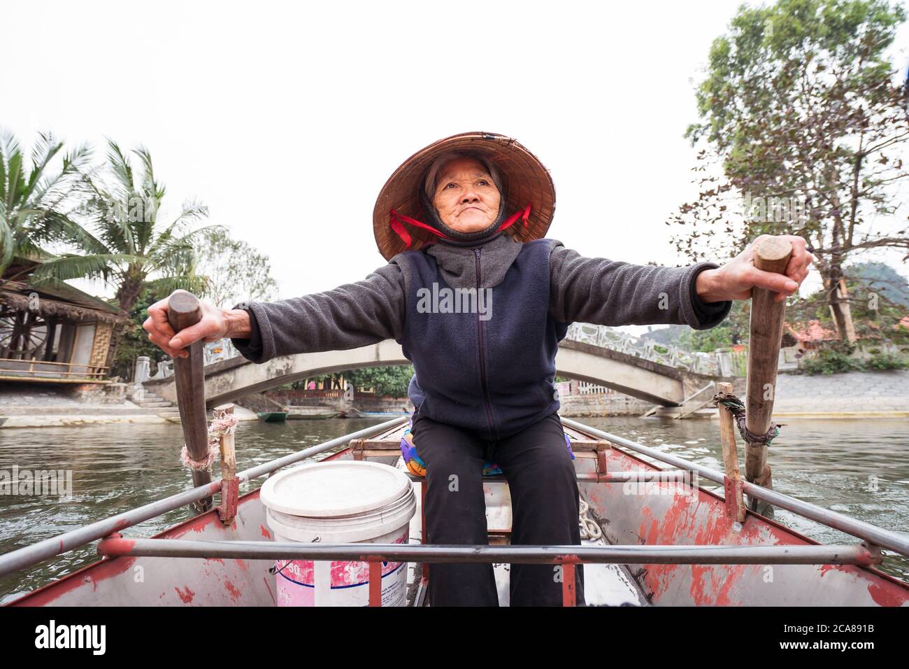 TAM Coc / Vietnam - 25. Januar 2020: Vietnamesische ältere alte Frau mit traditionellen Kegelhut Ruderboot mit Touristen im Naturpark Stockfoto