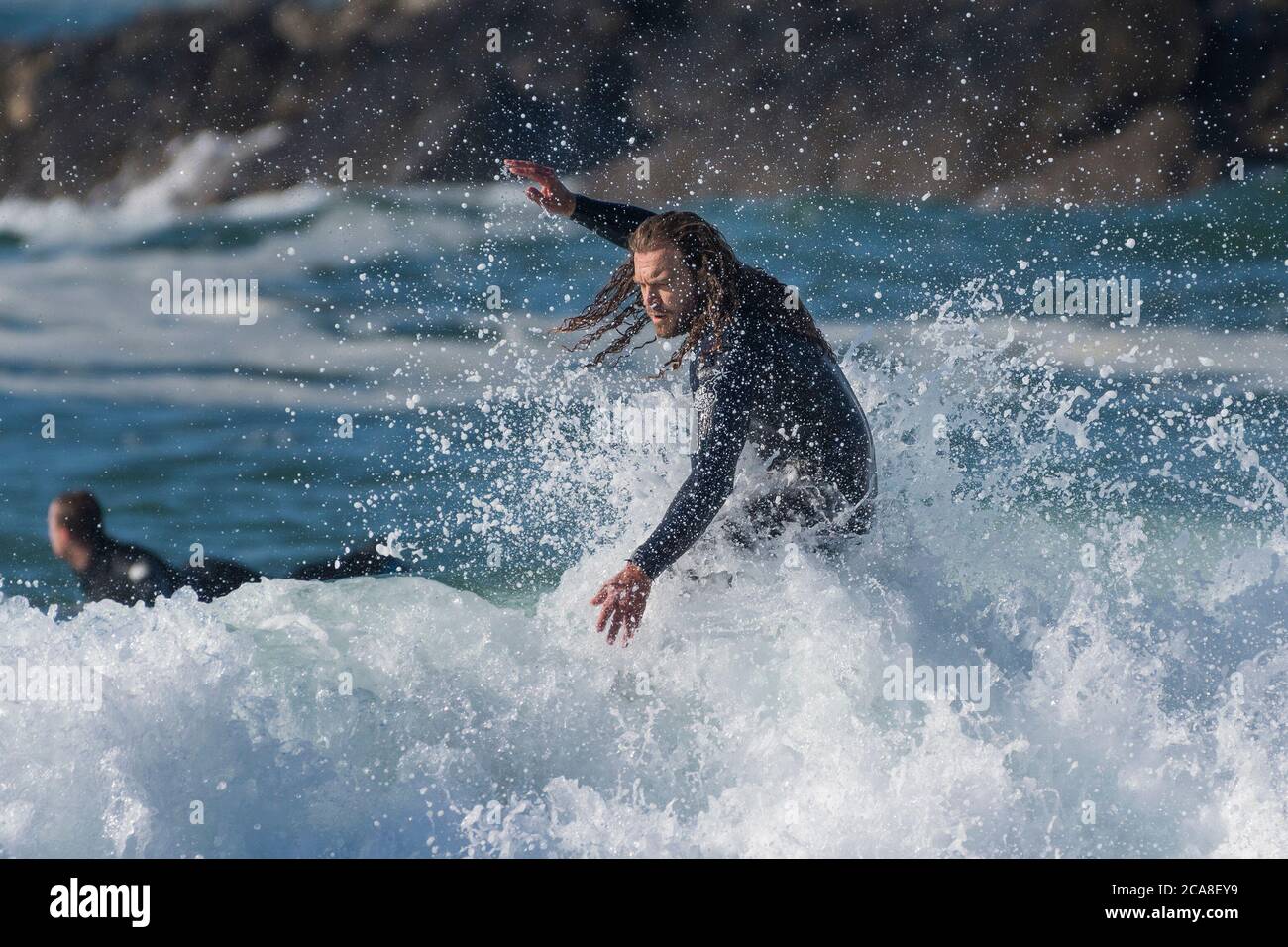 Spektakuläre Action als männlicher Surfer mit langen Haaren reitet eine Welle bei Fistral in Newquay in Cornwall. Stockfoto