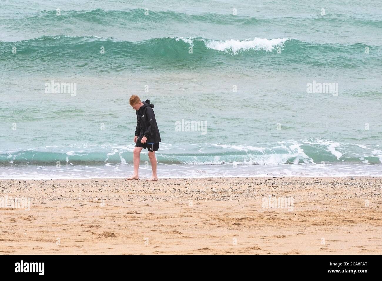 Ein junger männlicher Urlauber, der alleine am Fistral Beach in Newquay in Cornwall entlang geht. Stockfoto