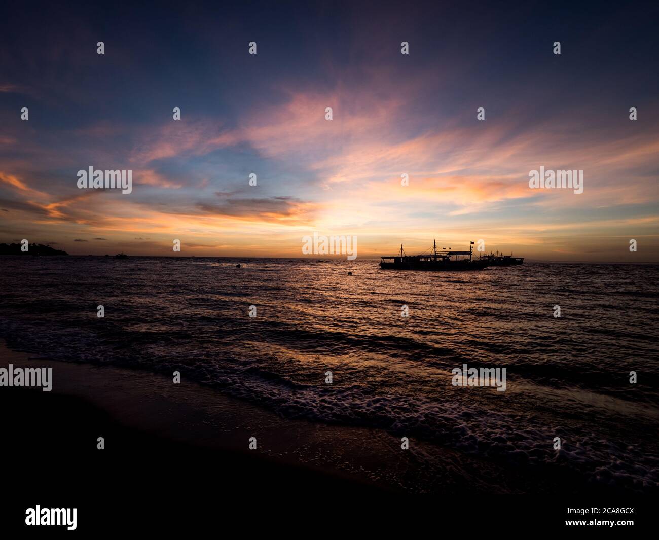 Atemberaubender Sonnenaufgang über dem Strand auf den Philippinen. Tauchboote warten auf Taucher am frühen Morgen. Stockfoto