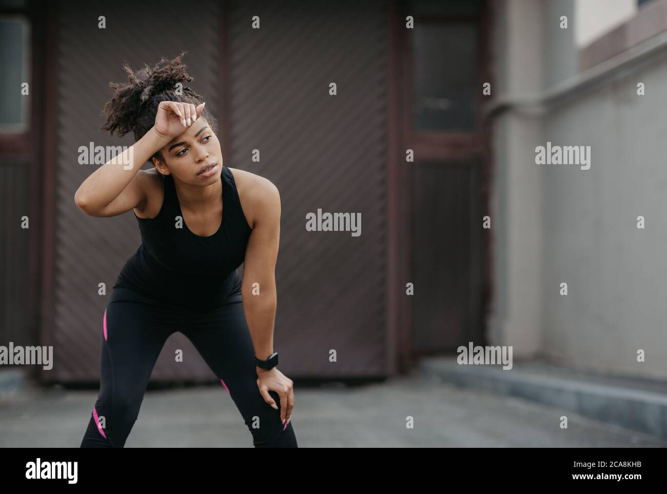 Ende des Rennens. Müde afroamerikanische Mädchen in Sportbekleidung mit Fitness-Tracker wischt Schweiß von der Stirn auf der Straße Stockfoto