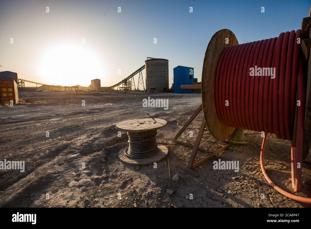 Goldindustrie und Produktion. Goldbergbau- und Verarbeitungsanlage. Roter Schlauch und Spule aus Kabeldraht und Silo mit Förderband bei Sonnenuntergang. Altynalmas compa Stockfoto