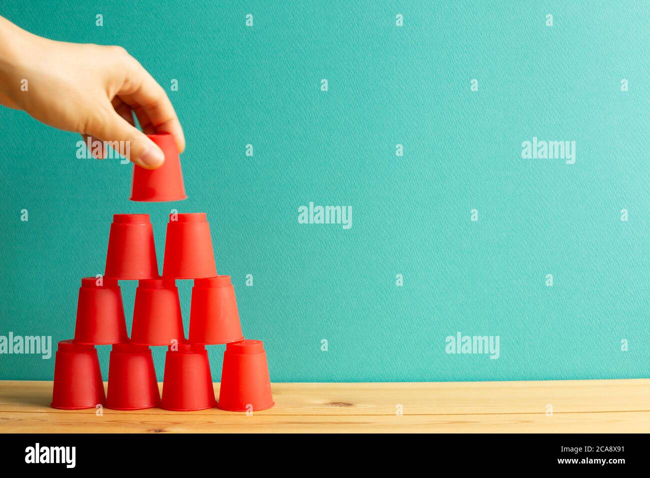 Pyramide aus roten Plastikbechern auf Holztisch mit grünem Hintergrund Stockfoto