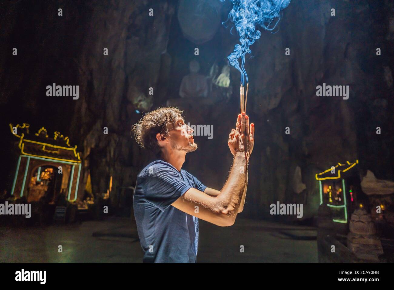 Junger Mann, der in einem buddhistischen Tempel betet und Weihrauch hält Huyen Khong Höhle mit Schreinen, Marmorberge, Vietnam Stockfoto