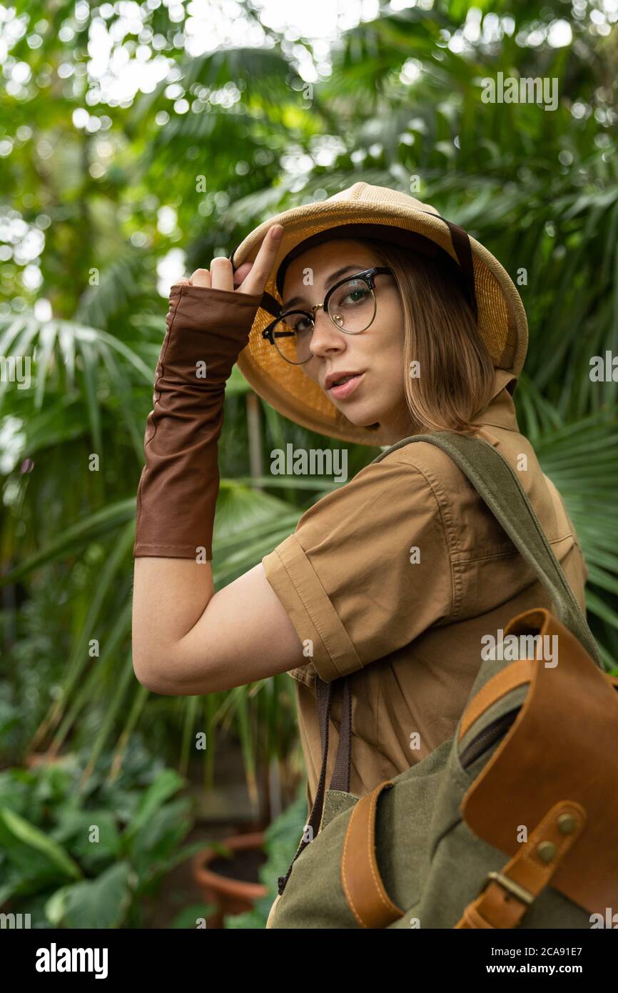 Frau Botanikerin im Safaristil im Gewächshaus gekleidet. Naturforscher in Khaki-Kleidung, Lever Handschuhe mit Rucksack Spaziergänge im Regenwald von p umgeben Stockfoto