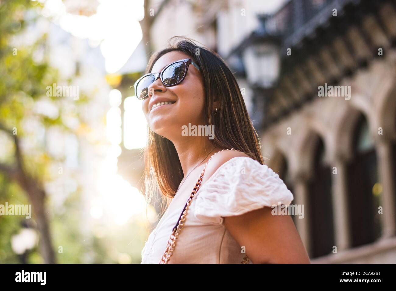 Frau mit Sonnenbrille lächelt, als sie durch die Stadt geht Stockfoto