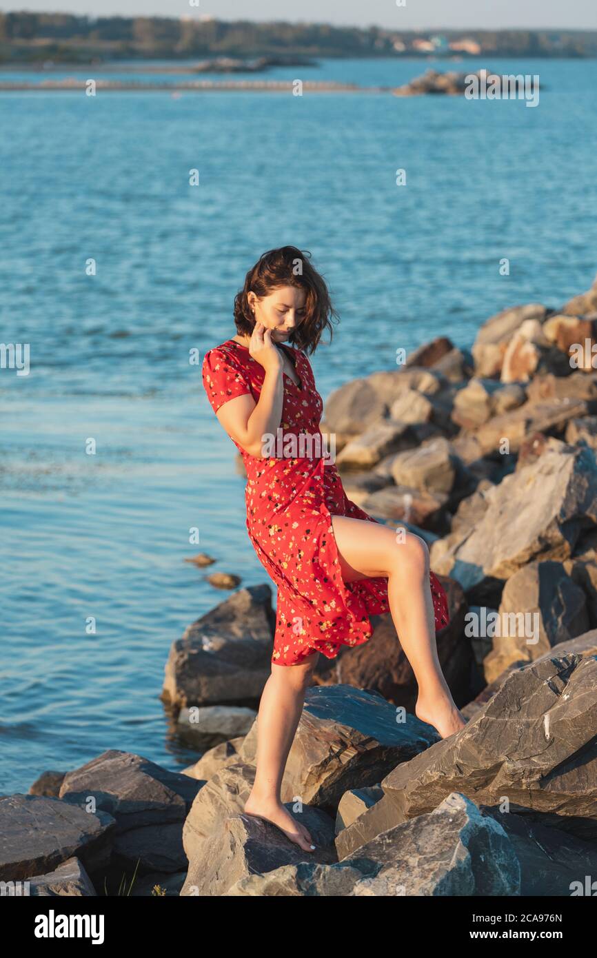 Junge schöne Frau in einem leichten lässigen roten Kleid ruht und posiert auf Felsen auf einem