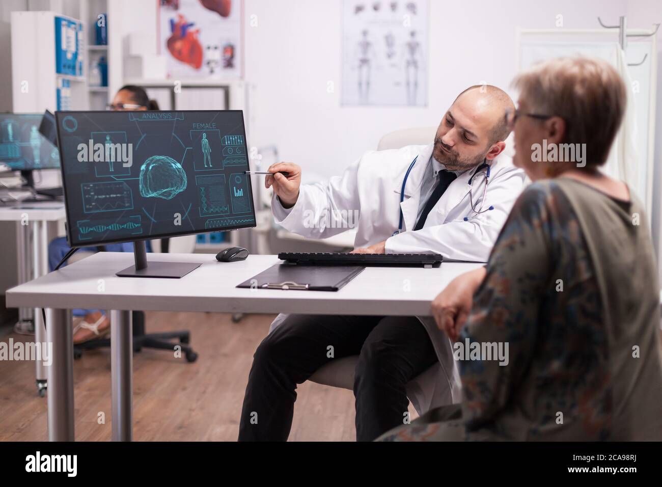 Arzt zeigt auf CT-Scan auf dem Computer für ältere Patienten während des Besuchs nach einer Hirnchirurgie. Diagnose für Kopftrauma. Medic trägt weißen Mantel und Stethoskop. Stockfoto