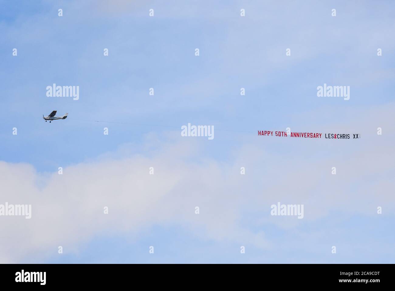 Banner abschleppen. Ein Cessna Leichtflugzeug schleppen ein Banner mit Angabe Happy 50th Anniversary Les & Chris, mit Küssen. Botschaft am Himmel feiern. G-ENEA Stockfoto