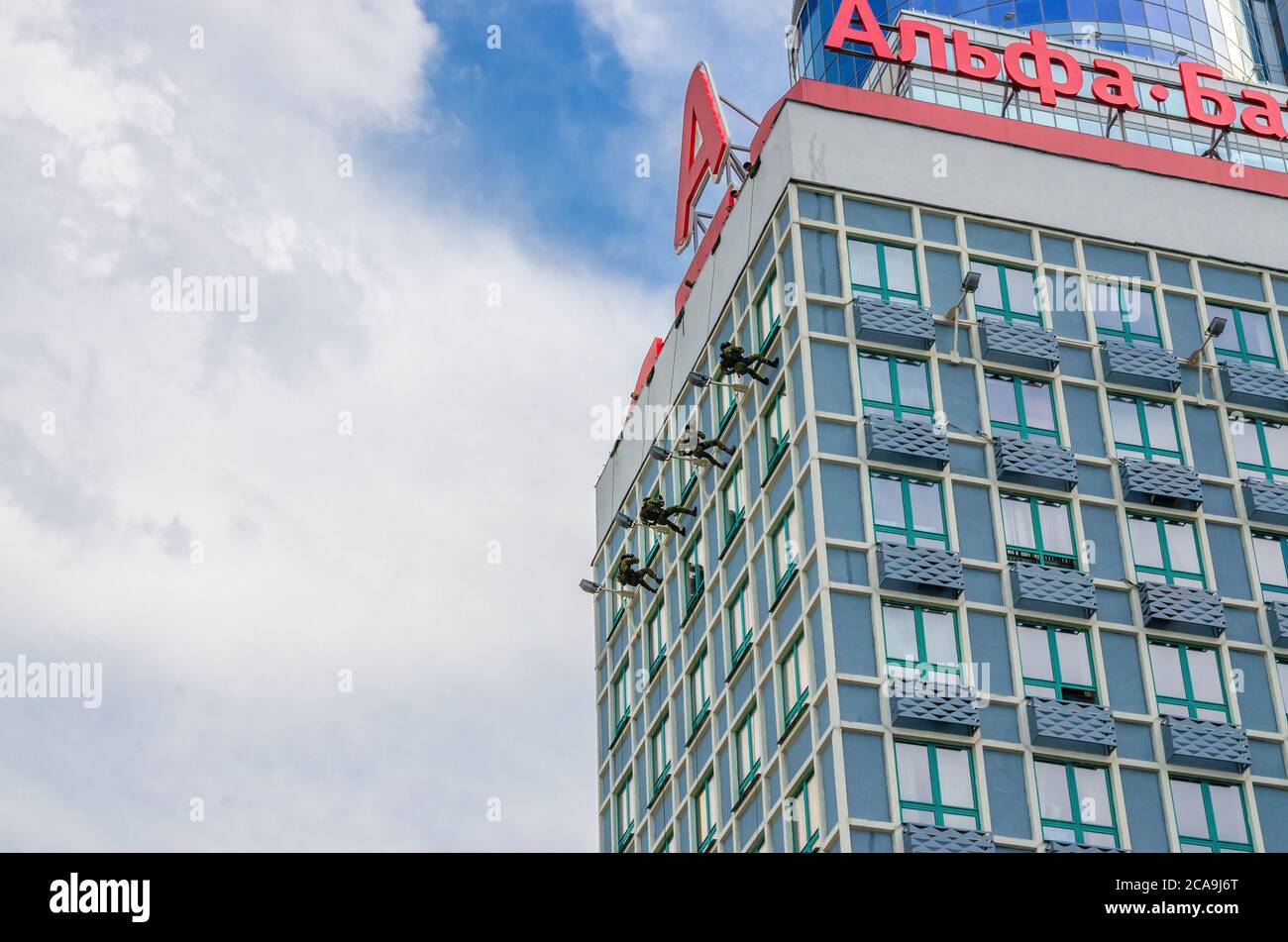 Minsk, Weißrussland, 26. Juli 2020: Die Soldaten der Spezialoperationen die Kräfte der weißrussischen Armee, die die Wand des Wolkenkratzers hoch zwischen den Fenstern klettern, der blaue Himmel weiß die Wolken am sonnigen Sommertag Stockfoto