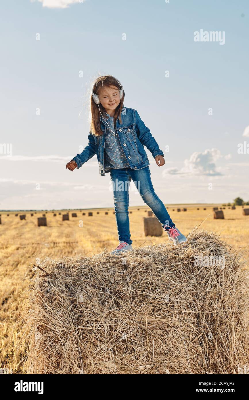 Ein nettes kleines Mädchen hört Musik und tanzt auf einem Heuhaufen. Hochwertige Fotos Stockfoto