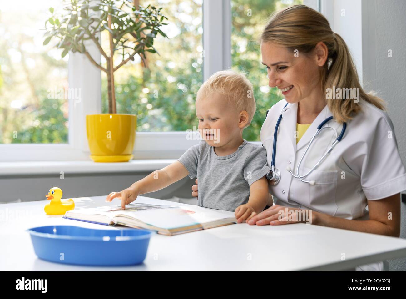 Angenehmer Arzt und Kind beobachten Buch zusammen am Schreibtisch in Klinik Büro. Kleiner Junge bei Kinderarzt Besuch Stockfoto