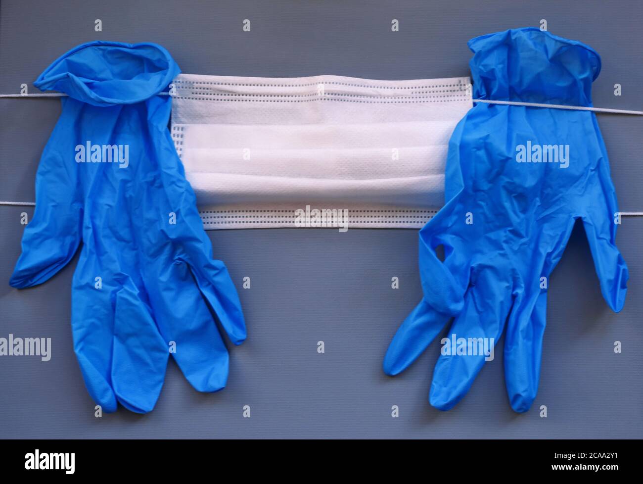 Paar medizinische blaue Latex Schutzhandschuh und weiße Maske auf grauem Hintergrund. Schutzausrüstung gegen Virus, Grippe, Coronavirus (COVID-19). Stockfoto