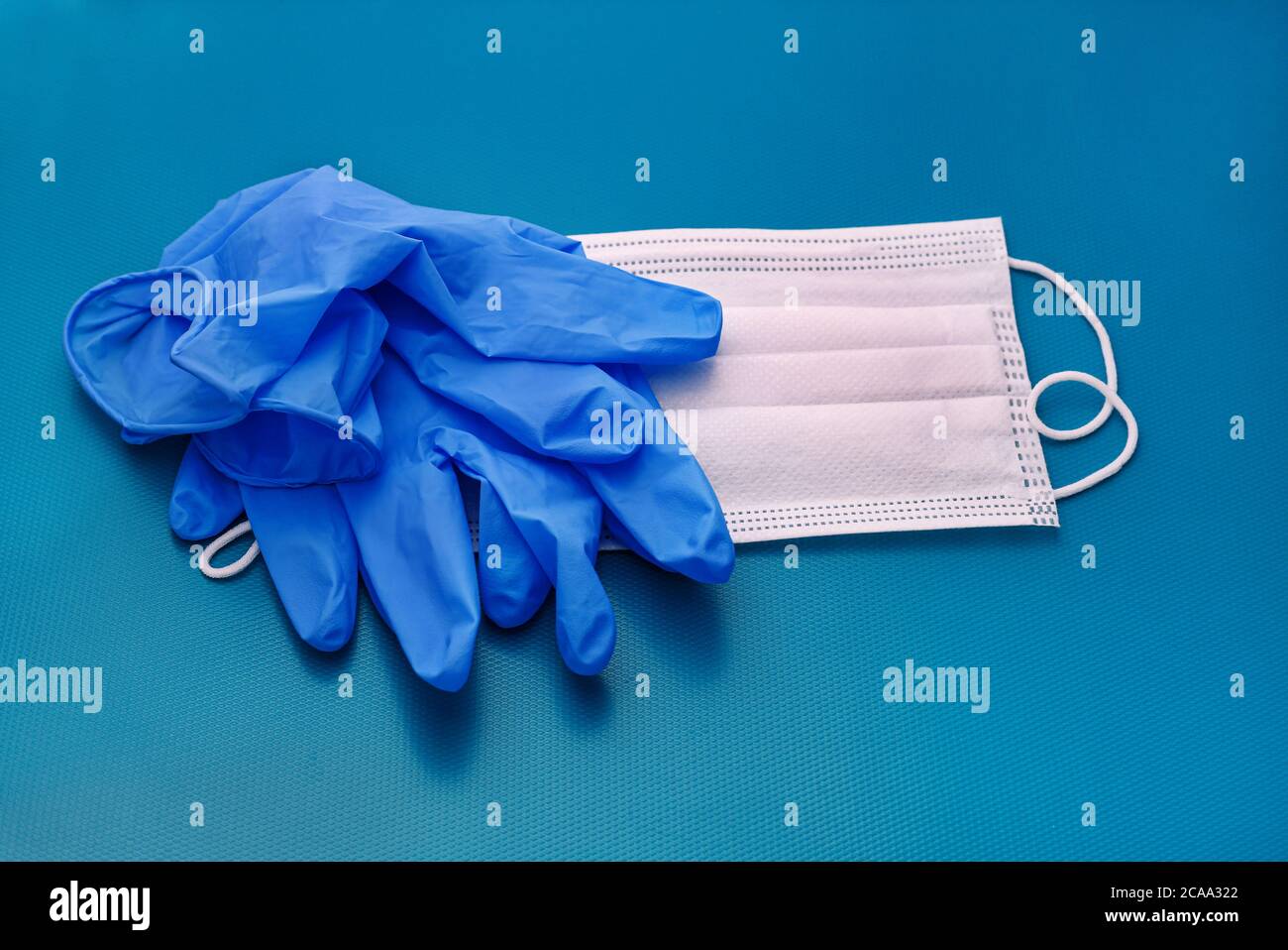 Paar medizinische blaue Latexschutzhandschuhe und weiße Maske auf blauem Hintergrund. Schutzausrüstung gegen Virus, Grippe, Coronavirus (COVID-19). Stockfoto