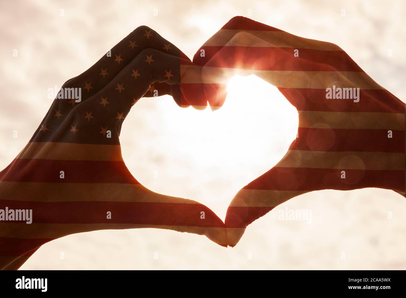 American USA Flagge Hand Herz Form Silhouette gegen die Sonne und den Himmel eines Sonnenaufgangs oder Sonnenuntergang gemacht Stockfoto