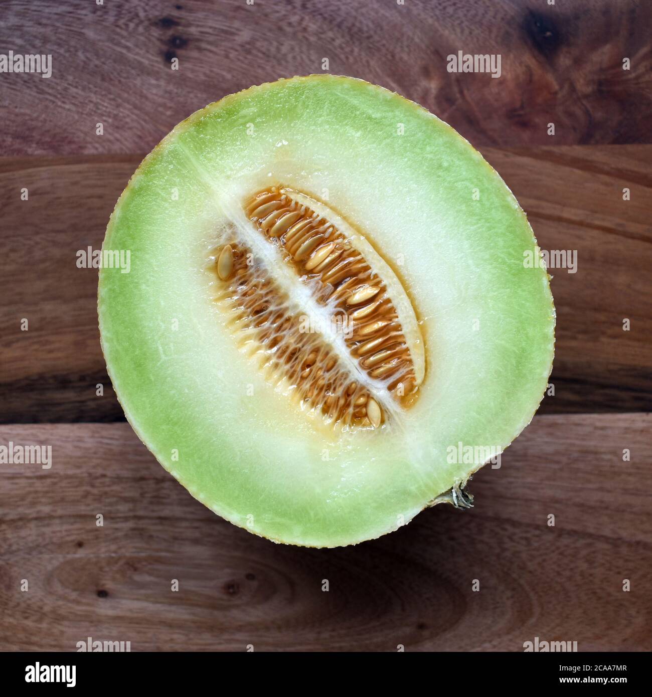 Frisches Galia Melone Obst halbiert Foto zeigt Samen und Fleisch auf einem Holzhintergrund unter natürlichem Licht. Appetitlich, ansprechend, einladendes Obst Stockfoto