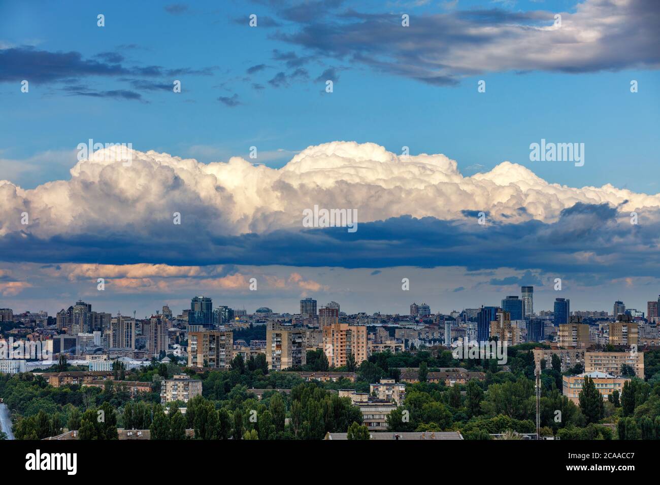 Sonnenstrahlen beleuchten die oberen Kappen weißer Wolken, die im Morgengrauen über der schlafenden Stadt hängen. Strahlendes Licht am dramatischen Morgenhimmel. Stockfoto