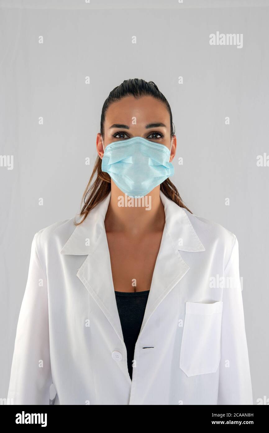 Attraktive Ärztin mit Virenschutzmaske Blick geradeaus und weißem Hintergrund. Stockfoto