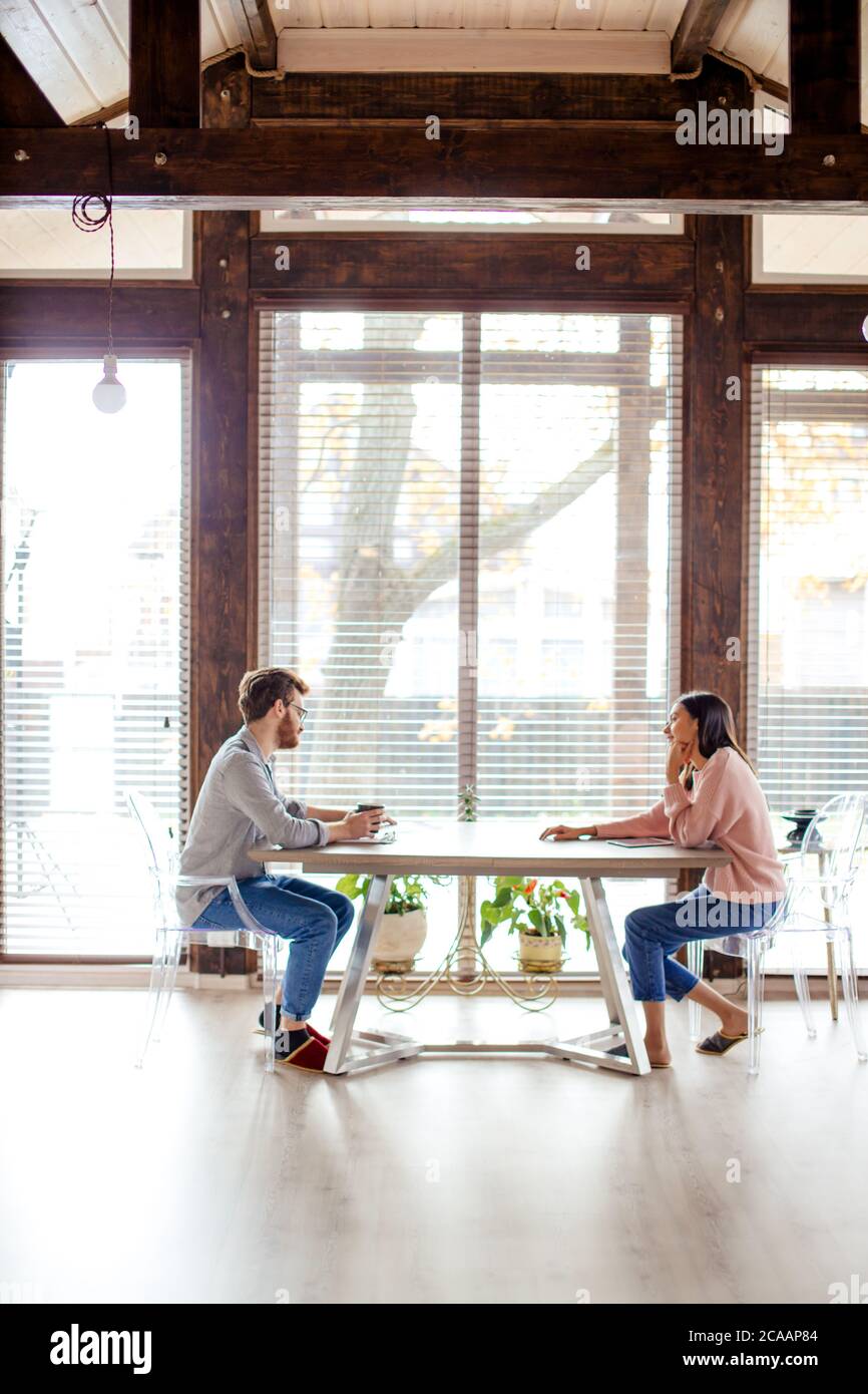 Panoramablick auf große geräumige Zimmer und kaukasischen Paar gegenüber am gleichen Tisch im Haus mit großen Fenstern im Hintergrund sitzen. Speicherplatz kopieren. Stockfoto