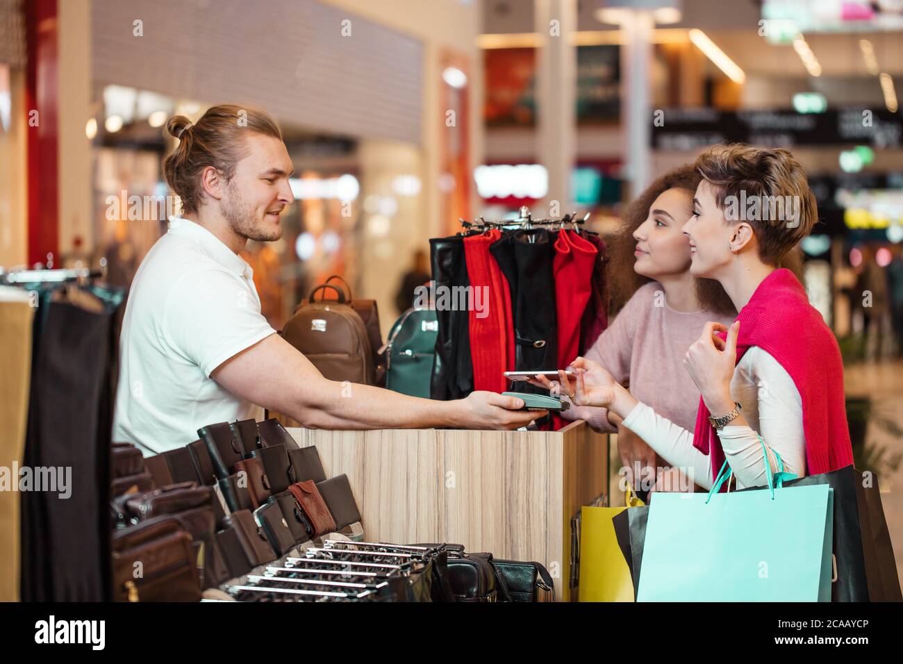 Weibliche Kunden zahlen für Lederwaren mit kontaktloser Kreditkarte mit der NFC-Technologie. die Verkäufe Person mit einem credit card reader Maschine bei einem Zähler Stockfoto