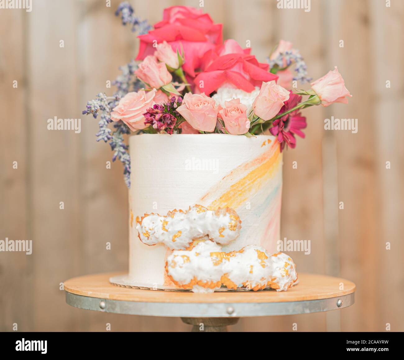Elegant dekorierter Regenbogen-Kuchen mit Cremepuffs und einem Blumenarrangement. Stockfoto