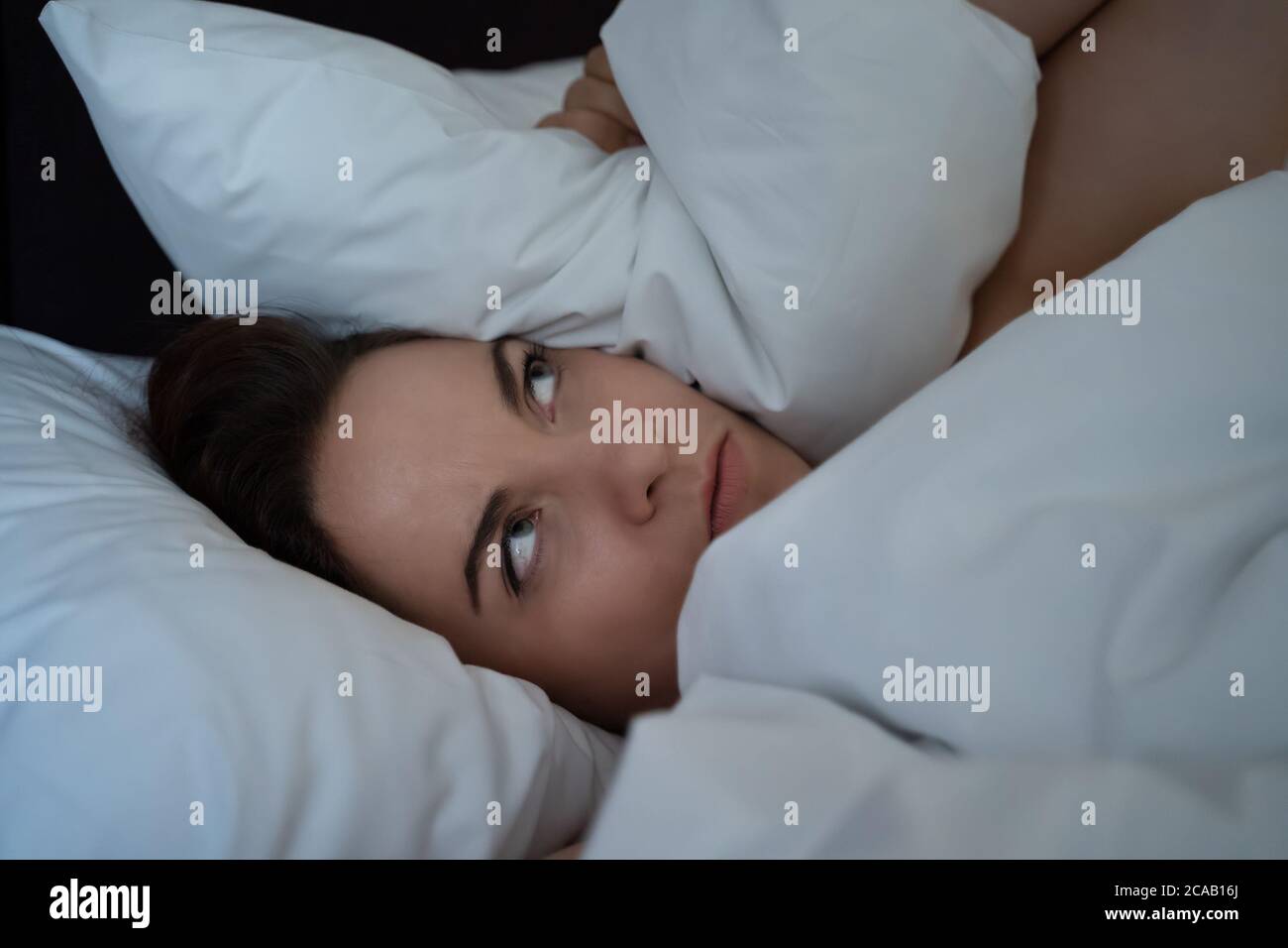 Junge Frau Schlaflosigkeit bedeckt Kopf mit Kissen, kann nicht schlafen vom Lärm der Nachbarn, unglücklich gestört frustrierten Person in der Nacht. Stockfoto