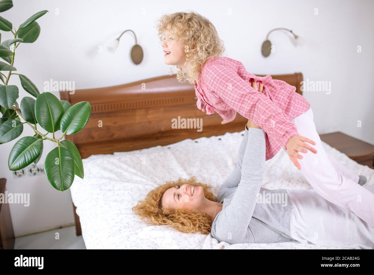 Schöne glückliche Mutter liegt auf dem Bett und die Erhebung ihrer Tochter suchen mit Zärtlichkeit. Liebeskonzept. Familie. Beziehungskonzept Stockfoto
