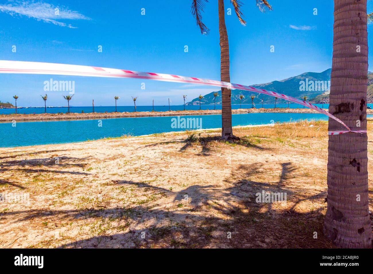 Quarantäne rot-weißes Band über exotischen schönen Strand mit klarem blauen Himmel. Urlaubskonzept, verspätetes Reisen, keine Sommerpläne mehr und keine Heimat mehr Stockfoto
