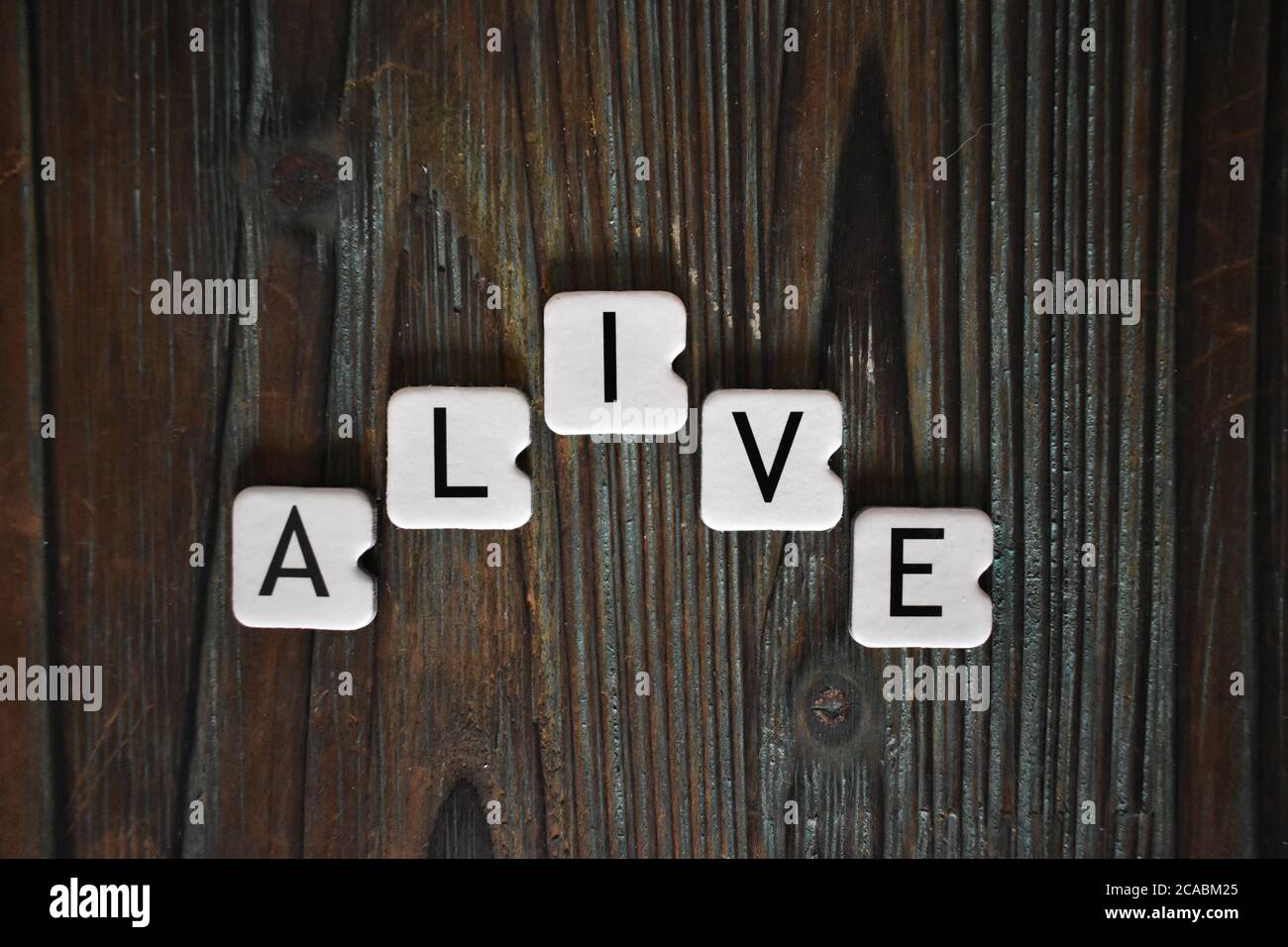 Nahaufnahme von quadratischen Buchstaben des Wortes 'lebendig' auf Ein strukturierter Holztisch Stockfoto