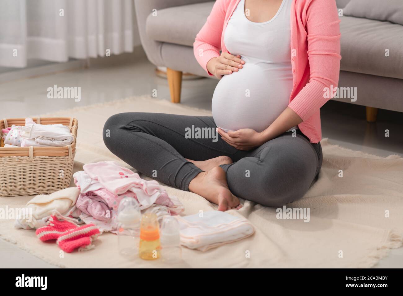 Schöne schwangere asiatische Frau Verpackung und Vorbereitung Babykleidung im Korb für werdende Neugeborene Stockfoto
