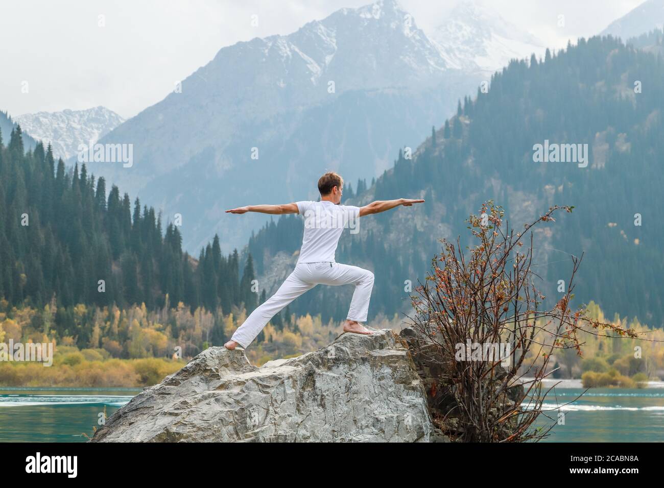 Yoga Mann in Krieger Pose auf Bergsee Felsen, ourodoor Aktivitäten Konzept. Stockfoto