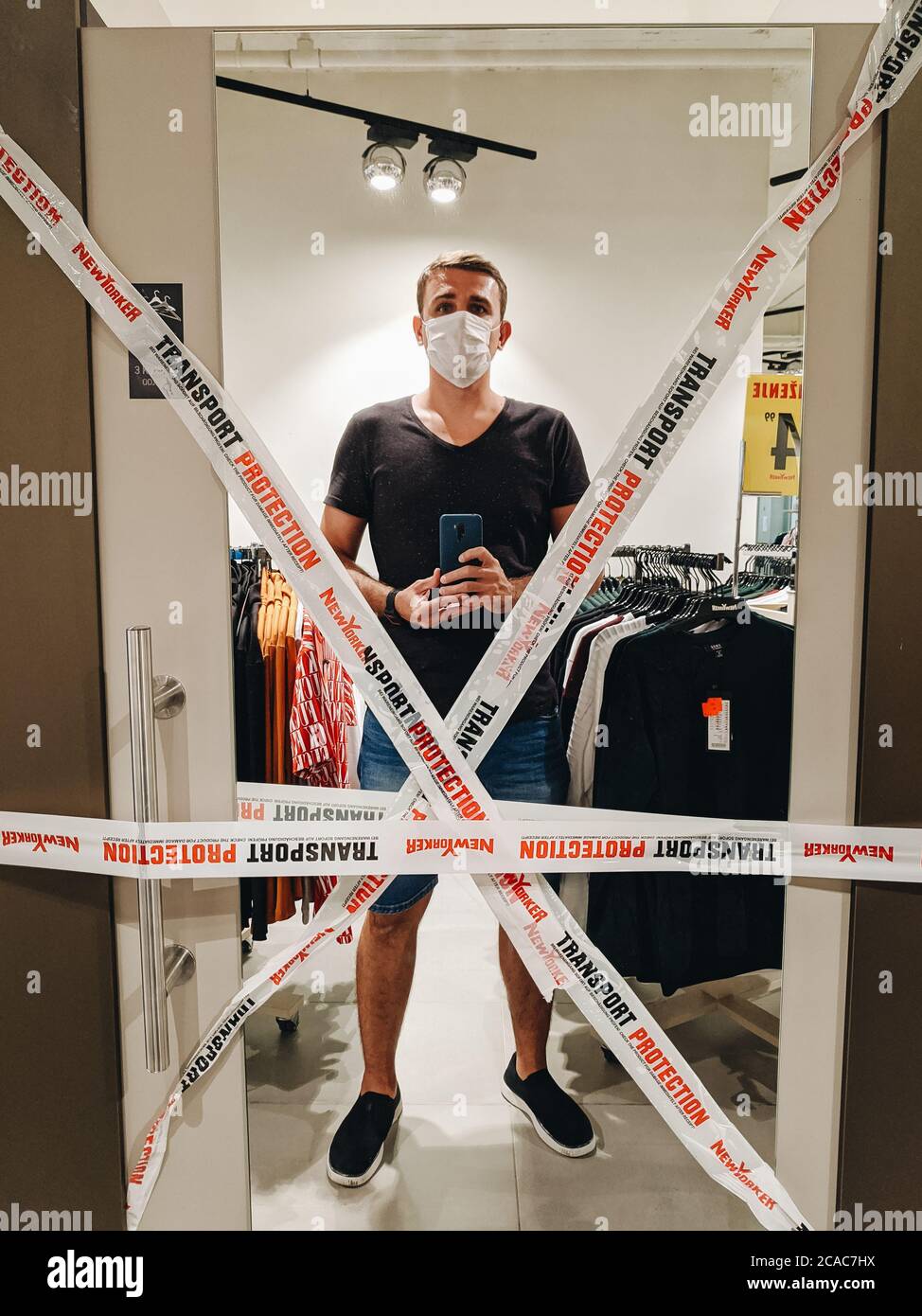 Budva, Montenegro - 01. august 2020: Ein Mann mit einer medizinischen Maske nimmt ein Selfie im Spiegel einer Garderobe in einem NewYorker Bekleidungsgeschäft, bedeckt Stockfoto