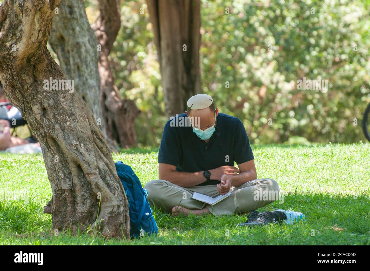 Freizeit unter COVID-19 Einschränkungen Menschen in einem Park mit Schutzmasken sitzen in einem Abstand zwischen den Gruppen und Einzelpersonen. Der Ausbruch von COVID Stockfoto