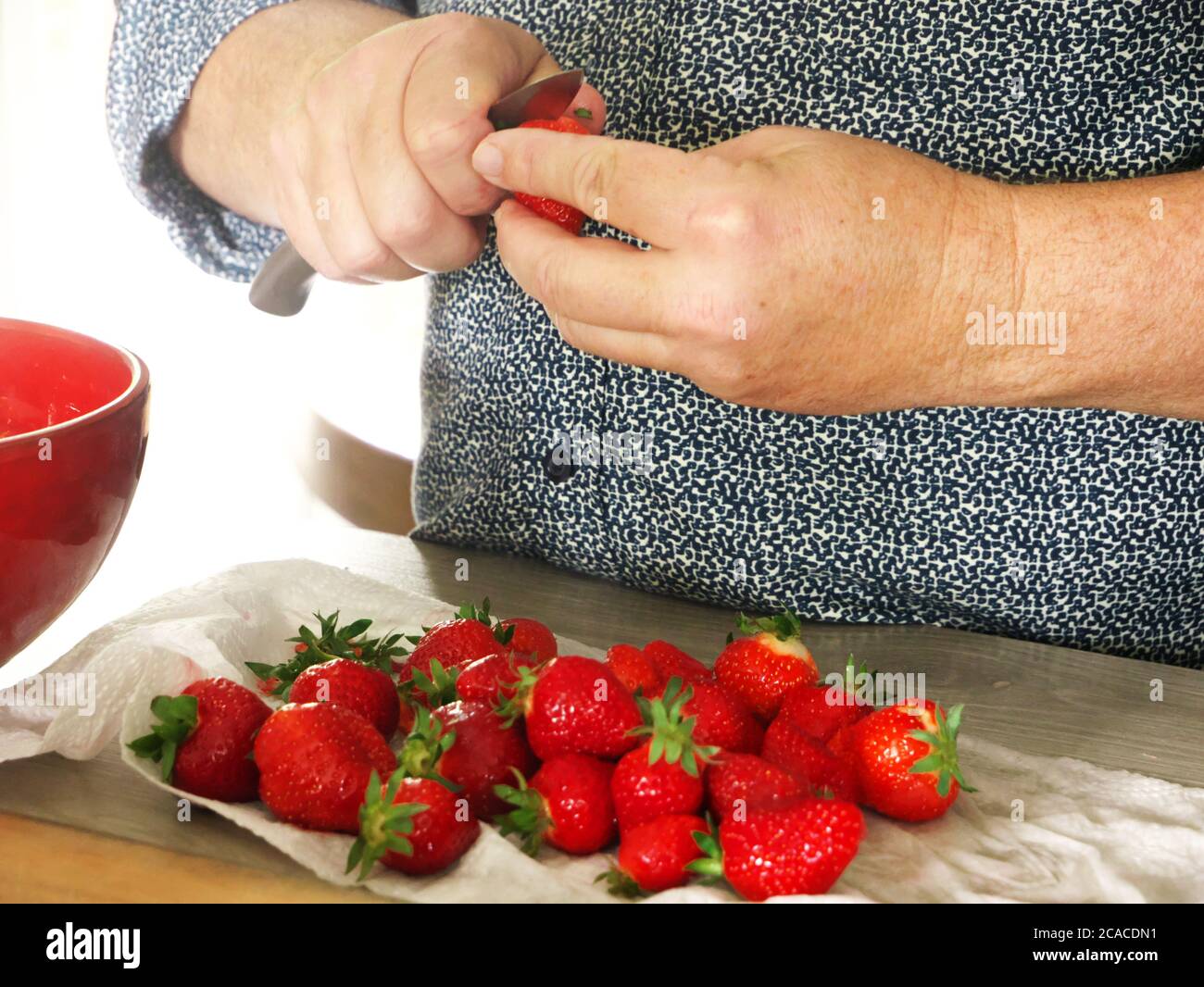 Nahaufnahme der Hände eines Mannes, der Erdbeeren schneidet. Ein Mann bereitet in der Küche ein erfrischendes Erdbeerdessert für seine Gäste zu Stockfoto