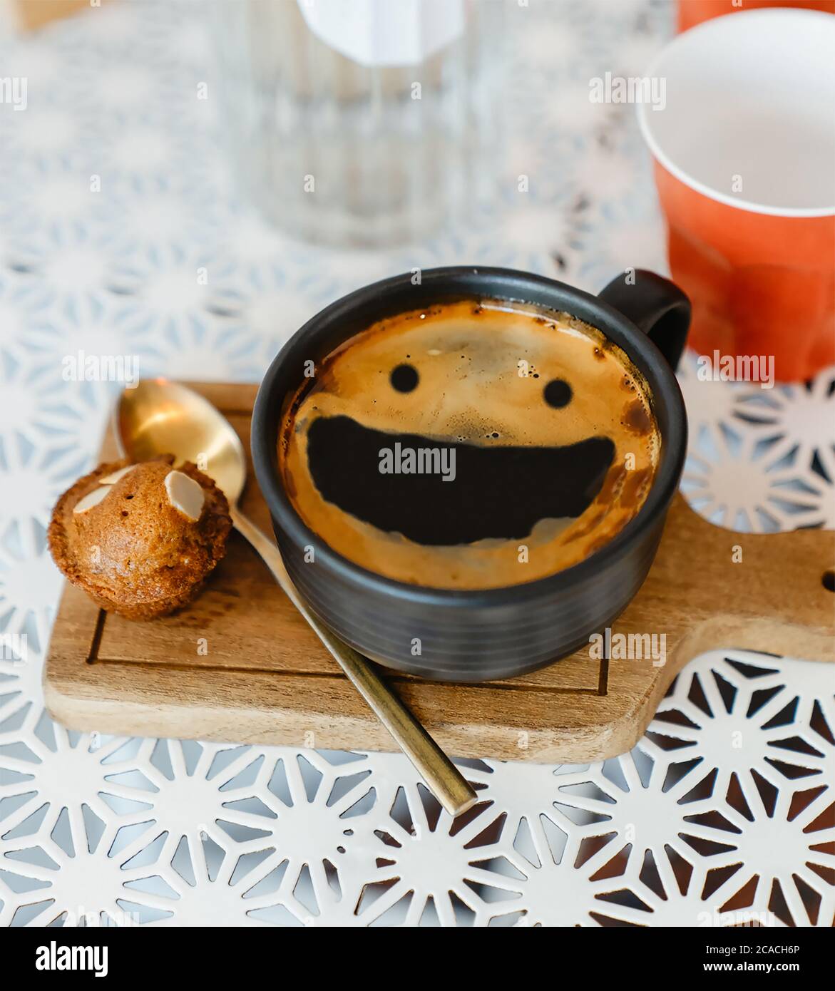 Draufsicht Smile Face Creama heißen schwarzen Kaffee in schwarzer Keramik Tasse auf Holztablett setzen weißen Tisch mit roten Plastikbecher und Glasflasche Wasser auf wh Stockfoto