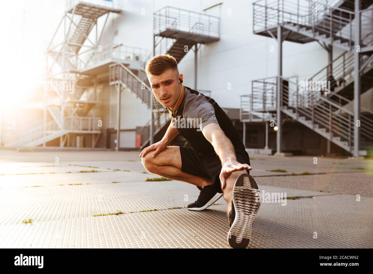 Bild von unrasierten kaukasischen Sportler in Kopfhörern, die Sport treiben, während sie im städtischen Bereich im Freien trainieren Stockfoto