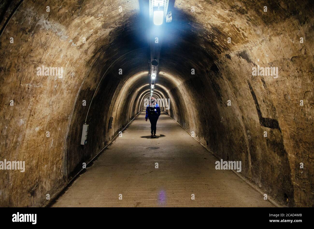 Eine junge Erwachsene Frau, die vor einem leeren Weg im Gric Tunnel in Zagreb, Kroatien, steht und von Leuchtstofflampen beleuchtet wird. Stockfoto