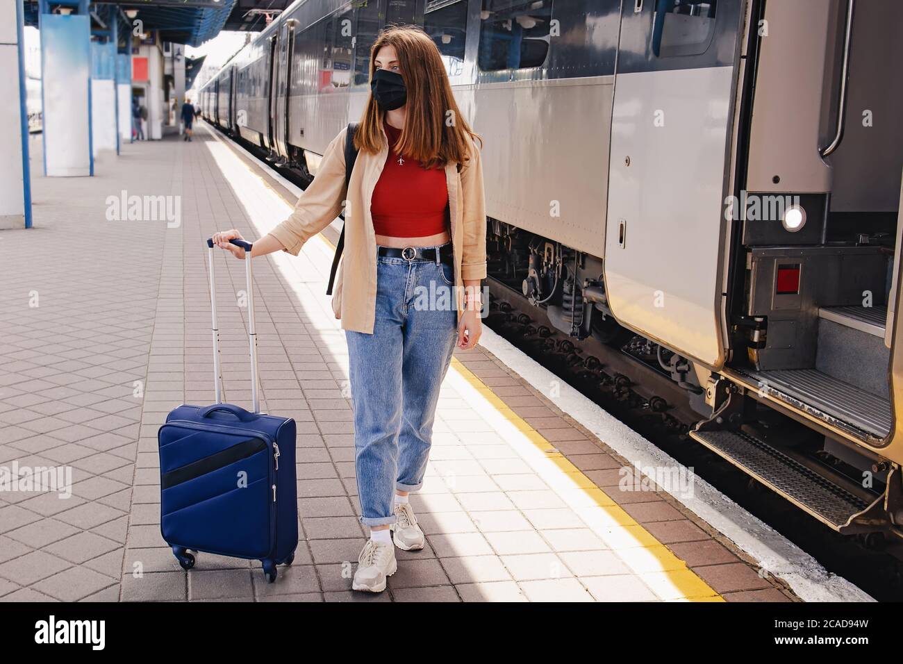 Frau in schützender Gesichtsmaske auf dem Bahnhof stehen In der Nähe des Zuges mit ihrem Koffer Stockfoto