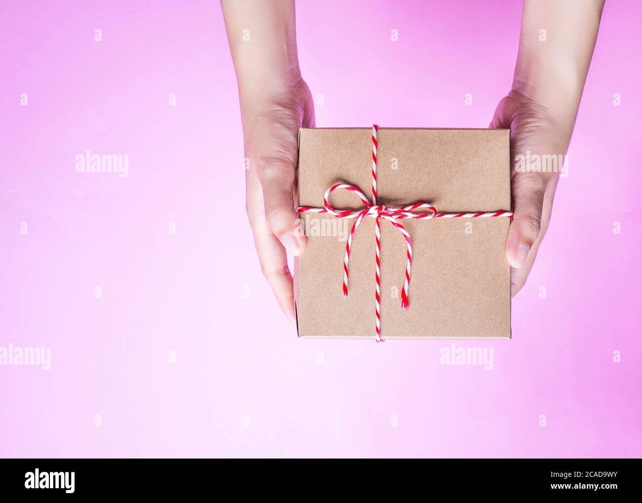 Weibliche Hände halten eine einfache Handwerk Papier Geschenkbox mit bunten Seil mit als Geschenk für Weihnachten, Neujahr, valentinstag oder Jubiläum verpackt Stockfoto