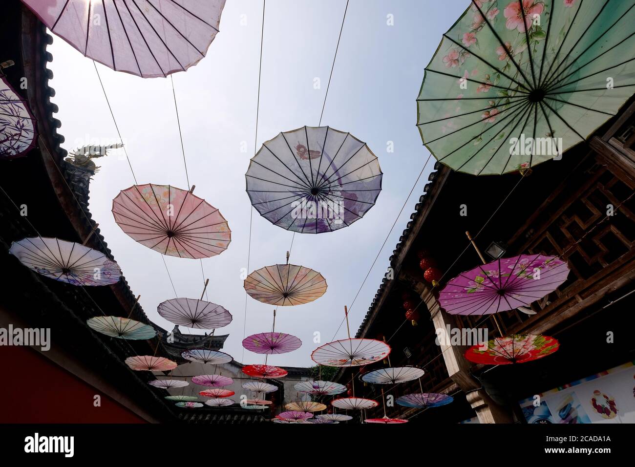 Viele geölte Papierschirme hängen in der alten chinesischen Stadt. Weitwinkel. Beliebtes chinesisches Kunsthandwerk Stockfoto