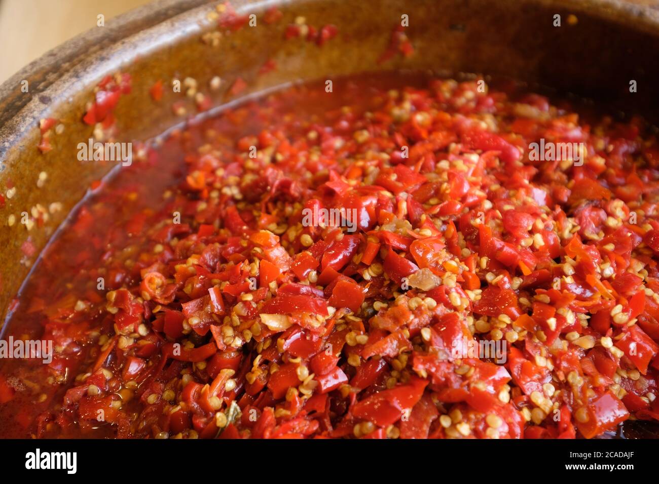 Nahaufnahme frisch gehackter Chilischote in braunem Keramikglas unter natürlichem Tageslicht. Beliebte chinesische Gerichte und Gewürze. Weichfokus Stockfoto