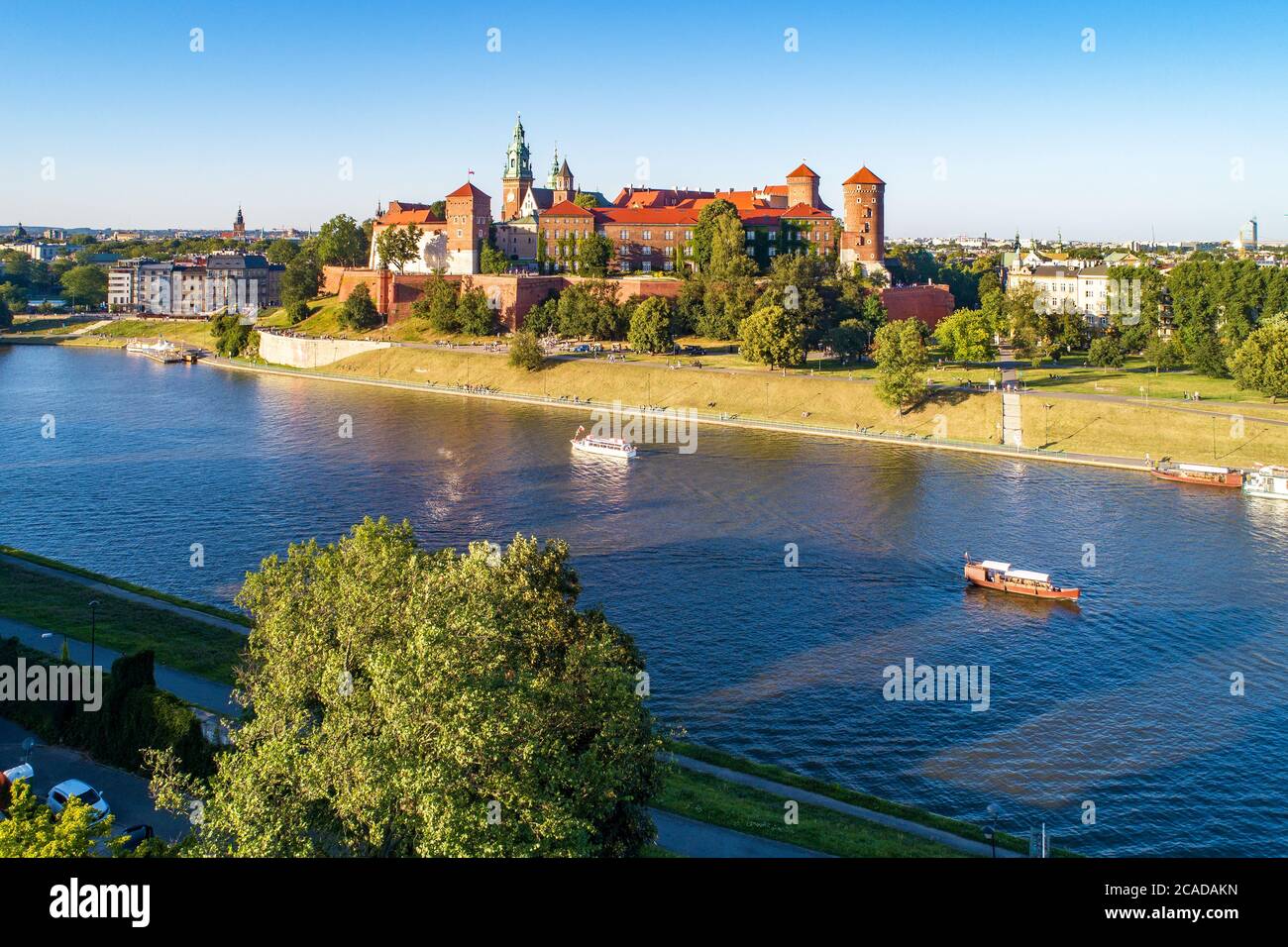 Königliche Wawel-Kathedrale und Schloss in Krakau, Polen. Luftaufnahme bei Sonnenuntergang. Weichsel, Touristenboote, Flussufer mit Parks, Bäume, Promenade Stockfoto
